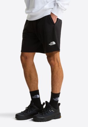 Shorts in cotone nero con cintura elastica e tasche laterali. Presentano un logo bianco sulla parte inferiore sinistra. Design semplice, senza motivi.