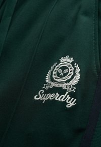 Mørkegrøn sportsjersey med tekstureret stof, broderet krone og tennisracketslogo, med "Superdry"-navnet i hvid.