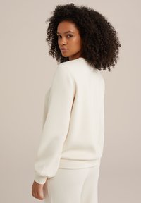 Krémová mikina s dlhými, priliehavými rukávmi a zaobleným výstrihom, s hladkou textúrou a voľným strihom.