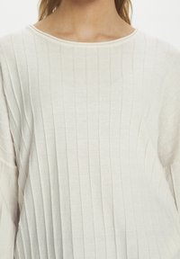 Cremfarbener Pullover mit vertikaler Rippstruktur, weitem Ausschnitt und langen Ärmeln. Weicher Stoff mit leicht lockerer Passform und minimalen Details.