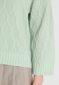 Ljus mintgrön stickad tröja med ett strukturerat diamantt mönster och ribbade ärmslut. Nederkanten är också ribbad för en extra detalj.