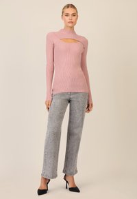 Rosa geripptes Langarmoberteil mit einem Ausschnitt-Design, kombiniert mit grauen Jeans mit gepunktetem Muster und schwarzen High Heels.