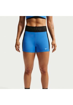 Atletisch persoon draagt blauwe Nike-shorts met zwarte tailleband en klein wit Nike-logo op het linkerbeen, staat met ontspannen armen.