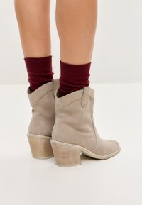 Botines de ante beige con un tacón alto y curvado y un diseño de costura, combinados con calcetines de punto burdeos.