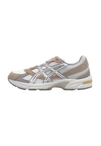 Zapatilla deportiva con parte superior de malla blanca, acentos de ante gris y detalles plateados. Cuenta con una suela acolchada y una puntera reforzada.