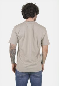 T-shirt in cotone beige con maniche corte, collo a giro e vestibilità rilassata. Presenta una texture liscia e leggeri dettagli sul colletto.