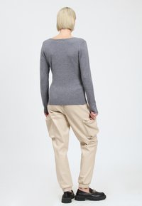 Maglione grigio a maglia con maniche lunghe, abbinato a pantaloni cargo beige in ecopelle con tasche laterali e scarpe nere slip-on.