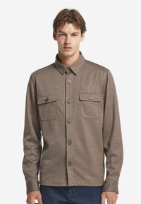 Brun skjorta med knappar, långärmad, med två bröstfickor och en klassisk krage. Tyget har en subtil textur.