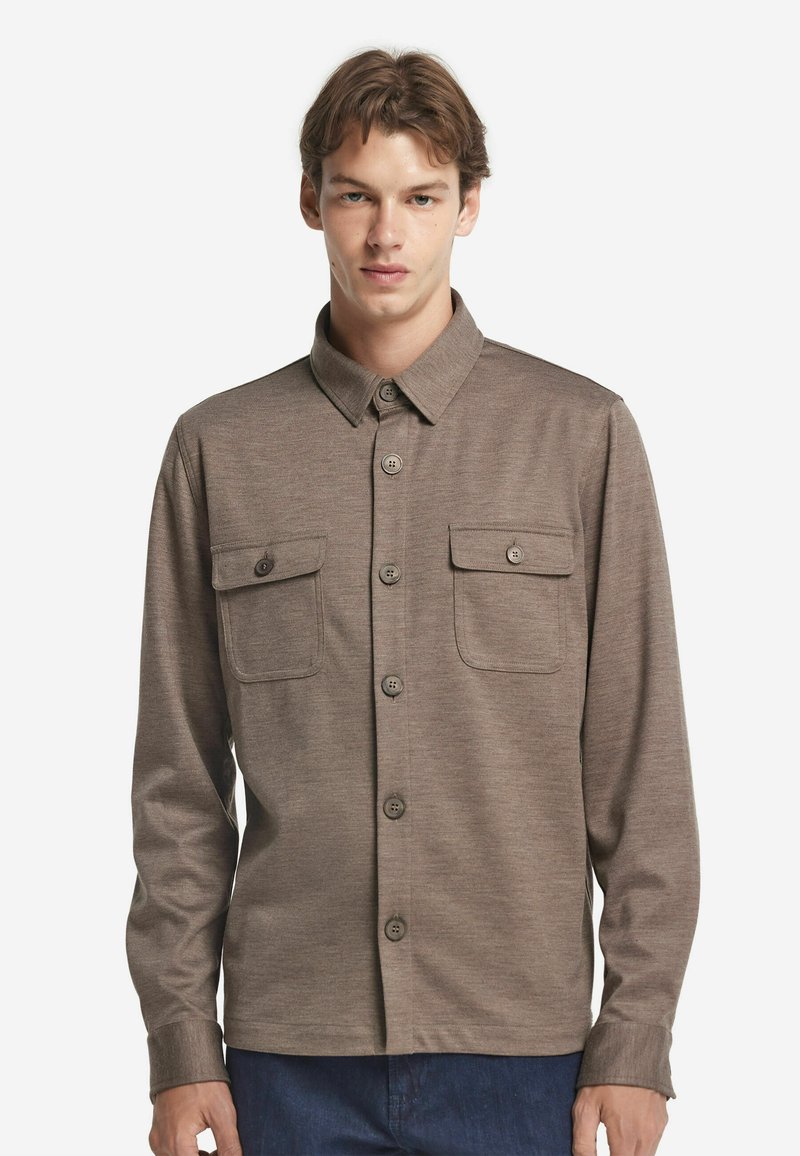 Brun skjorta med knappar, långärmad, med två bröstfickor och en klassisk krage. Tyget har en subtil textur.