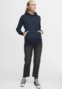 Sweatshirt à capuche bleu marine avec un motif à pois, deux poches avant et des accents en bois. Associé à un jean cropped noir et des baskets montantes noires.