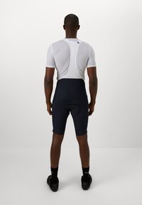 Haut à manches courtes en maille blanche associé à un short de vélo bleu marine avec rembourrage. La tenue présente une coupe élégante et un design minimaliste.