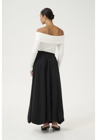 Bijela bluza na off-the-shoulder s dugom crnom suknjom s elastičnom talijom. Suknja ima glatku teksturu i lepršavi siluetu.