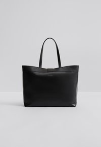 Μαύρη τσάντα ώμου από δέρμα με επίπεδες λαβές, μινιμαλιστικό σχέδιο, λεία υφή και κεντρικό διακοσμητικό στοιχείο με το όνομα της μάρκας.