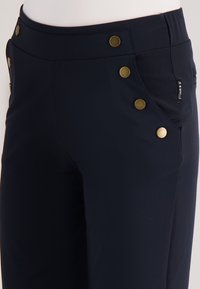 Marineblauwe broek met een aansluitend ontwerp, voorzien van vijf gouden knopen langs de taille en zijzakken. Gemaakt van een gladde, rekbare stof.