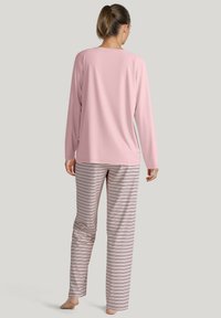 Roze langemouwen top met een ronde hals, gecombineerd met gestreepte pyjamabroek in zachte stof met horizontale lijnen in roomkleur en donkere kleuren.