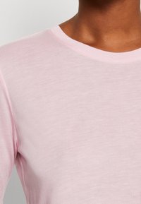 Top manica lunga rosa chiaro con scollo rotondo, caratterizzato da una texture liscia a costine e un design aderente. Vista ravvicinata del tessuto.