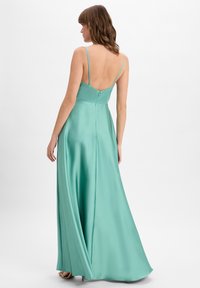 Ein mintgrünes Satin-Kleid mit einem tiefen Rückenausschnitt, dünnen Trägern und einem fließenden Rock, der einen seitlichen Schlitz und einen verdeckten Reißverschluss hat.