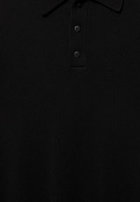Polo en maille noire avec col court et trois boutons noirs sur la patte de boutonnage, montrant les détails du tissu texturé.