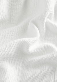Tissu tricoté blanc avec un motif en zigzag texturé et répétitif, et des plis doux créant des ombres délicates.