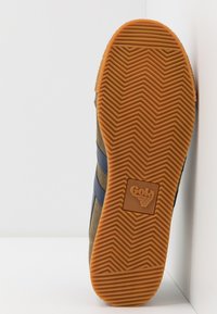 Gola sneakersula med ett fiskbensmönster, orange gummi och en beige mockaövre med blå ränder och logodetaljer på hälen.