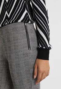 Black and white striped sweater worn with gray checkered pants featuring a side zip detail, highlighting contrasting textures and patterns.