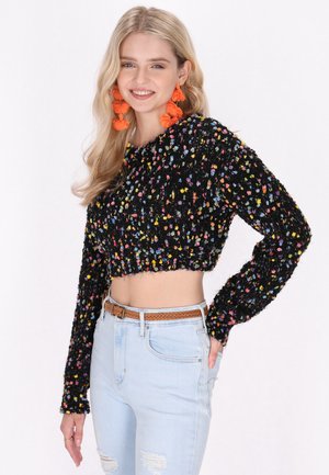 Maglione cropped nero con fiocchi colorati, superficie testurizzata, maniche lunghe, abbinato a jeans chiari strappati e una cintura intrecciata.