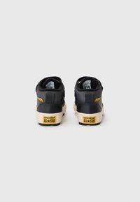 Baskets montantes noires en cuir texturé, avec des semelles en caoutchouc blanches et un logo jaune "Converse All Star" à l'arrière. Accents de design subtils.