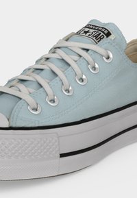 Ανοιχτού μπλε χαμηλό παπούτσι Converse All Star με λευκά κορδόνια και χοντρή λευκή σόλα με μαύρη ρίγα, κοντινή προβολή.