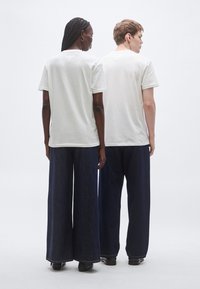 Άσπρα βαμβακερά μπλουζάκια και σκουρόχρωμο τζιν παντελόνι με φαρδιά πόδια, από πίσω όψη. Το μπλουζάκι έχει κοντά μανίκια και άνετη εφαρμογή.