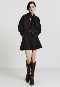 Cardigan in misto lana marrone con vestibilità oversize e grandi bottoni, abbinato a una gonna a campana coordinata e stivali alti in pelle marrone con tacco.