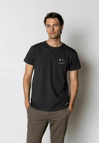 T-shirt en coton noir à manches courtes et col rond. Présente un graphique blanc d'un visage souriant sur le côté gauche de la poitrine.
