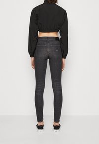 Černá zkrácená bunda přes tmavě šedé skinny džíny. Džíny mají zadní kapsy a jemnou texturu. Model má na sobě černo-bílé tenisky.