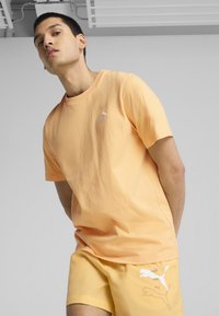 T-shirt in cotone color pesca con scollo rotondo e maniche corte; presenta un discreto logo bianco Puma sul lato sinistro del petto.