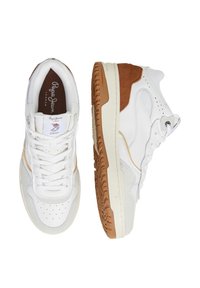 White sneakers with suede accents in tan and beige, textured rubber sole, perforated toe box, and laces. Brand logo on tongue.