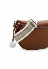 Hnědá kožená kabelka přes rameno s zakřiveným tvarem, vybavená proužkovaným látkovým popruhem v béžové, bílé a šedé barvě. Přítomné stříbrné logo a detaily na zipu.