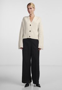 Κρεμ ανοιχτόχρωμο, κοντό καρντιγκάν με V-λαιμόκοψη και τρία μεγάλα καφέ κουμπιά. Συνδυασμένο με μαύρες παντελόνες ψηλόμεσες. Ομαλή υφή.