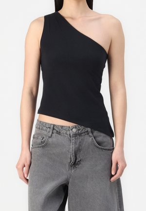 Woman wearing a black one-shoulder sleeveless top paired with high-waisted faded gray jeans against a plain background.