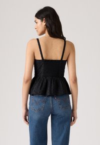 Svart peplum-topp med tynne stropper, teksturert stoff med smocking bak, kombinert med blå høytaljede jeans.