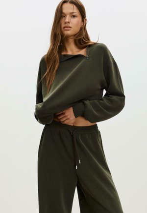 Olivengrüner, verkürzter Sweatshirt mit einem Reißverschluss am Hals, kombiniert mit passenden, locker sitzenden Sweatpants mit einem Kordelzug in der Taille.
