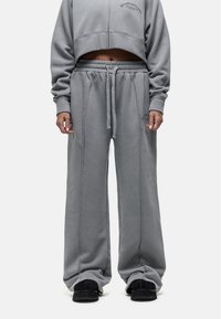 Jasnoszara krótkowana bluza z długim rękawem oraz pasujące szerokie spodnie dresowe z miękkiego materiału, z elastycznym pasem i sznurkiem. Widoczne szczegóły przeszyć.