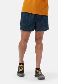 Marineblaue Badeshorts mit abstrakten blauen und orangefarbenen Mustern, mit Kordelzugbund und Logodetail auf der linken Seite, kombiniert mit grauen Schuhen.