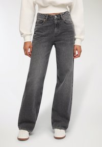 Jeans a vita alta e gamba ampia in denim nero sbiadito, con un classico design a cinque tasche e cuciture a vista.