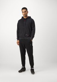 Zwarte hoodie met een textuurafwerking, voorzak en logodetail. Gecombineerd met zwarte sweatpants en voetbalschoenen, voorzien van een zijzak.