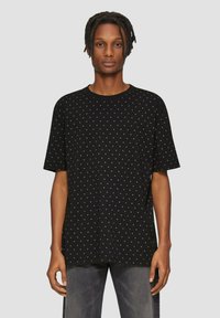 Zwart T-shirt met een comfortabele pasvorm, voorzien van een verspreid stippenpatroon in lichtere tinten. Korte mouwen en ronde halslijn.