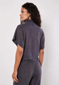 Grauer, weicher Strickpullover mit kurzen Ärmeln und hohem Kragen, der eine lockere Passform und eine glatte Textur aufweist. Insgesamt lässiges Design.