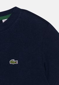 Marinblå bomulls t-shirt med rundad halsringning och korta ärmar, som har en liten grön och vit broderad krokodil-logotyp på bröstet.