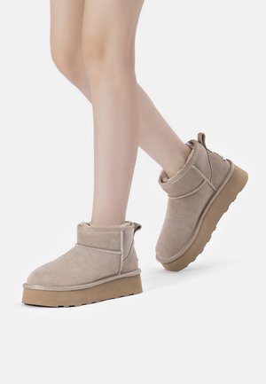 Beige Wildleder-Ankle Boots mit einem weichen Innenfutter, flacher Gummisohle und gesteppten Akzenten. Das Design verfügt über einen umgeschlagenen oberen Rand und eine Zuglasche.
