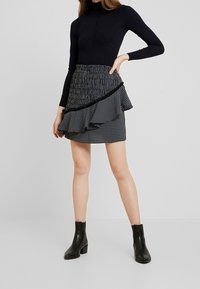 Haut noir à manches longues associé à une mini-jupe à volants et motifs. La jupe présente un tissu froncé, avec une bordure et un ourlet noirs contrastés.