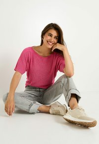 Top de punto rosa de manga corta con un escote amplio, combinado con pantalones vaqueros gris claro con puños y zapatillas beige con acentos texturizados.
