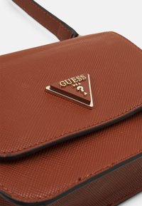 Bruine synthetische handtas met een gestructureerde afwerking, driehoekig logo van goudkleurig metaal en een enkele schouderband. Sluiting met klepontwerp en contrasterende randen.